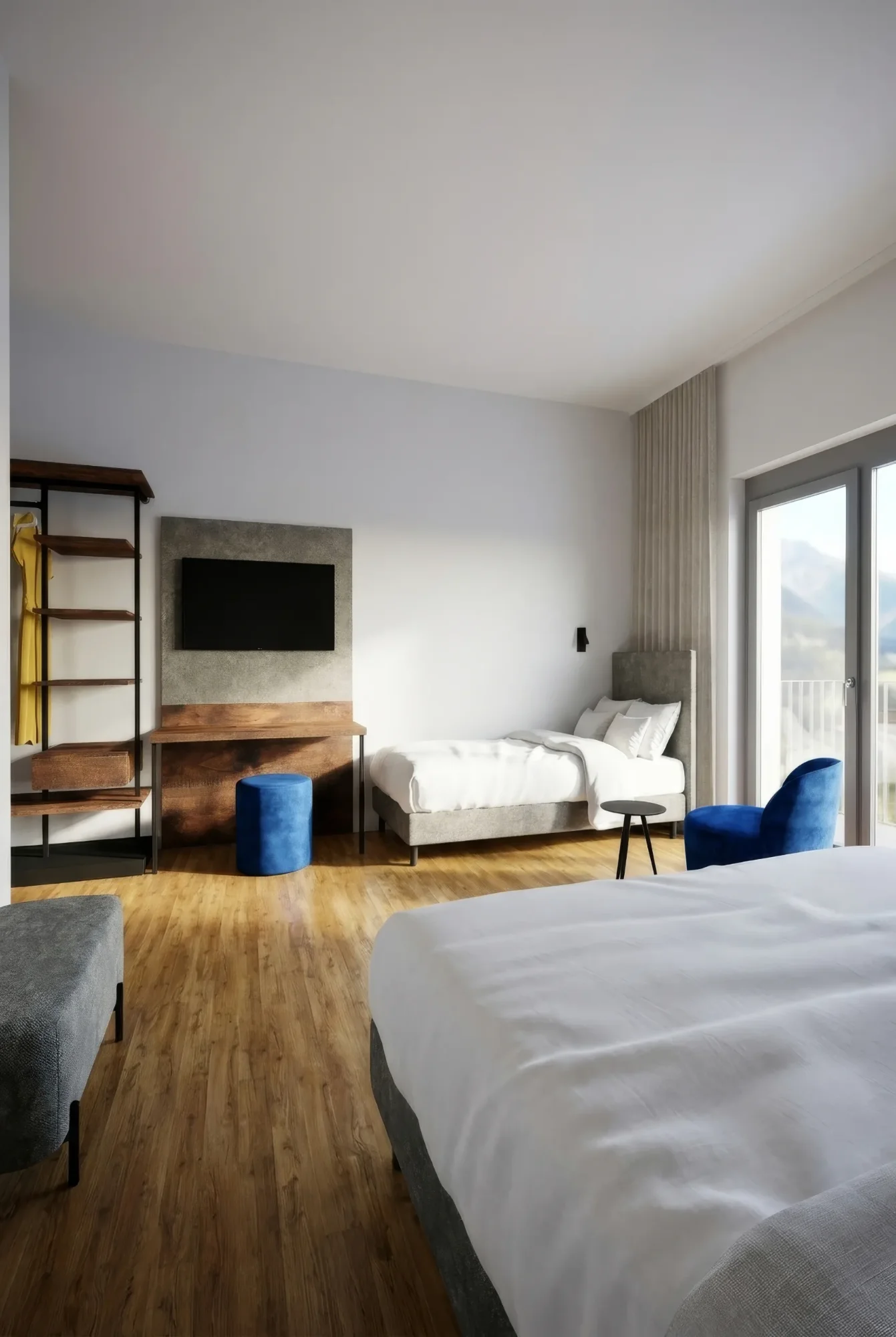 Modernes Hotelzimmer mit zwei Betten, Holzfußboden, TV, Schreibtisch und großem Fenster mit Bergblick. Akzente in Blau.