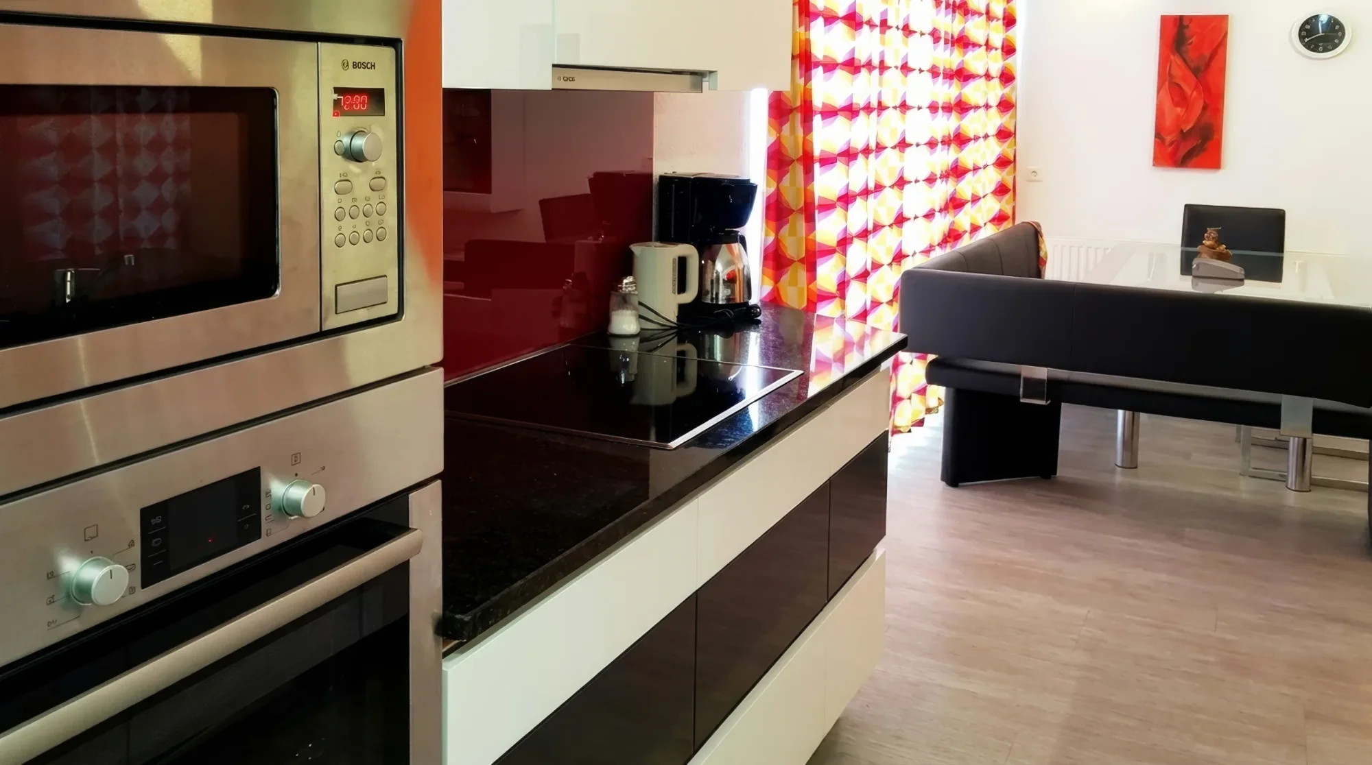 Moderne Einbauküche mit Edelstahl-Geräten, Induktionskochfeld, Kaffeemaschine und Essbereich mit schwarzer Eckbank.