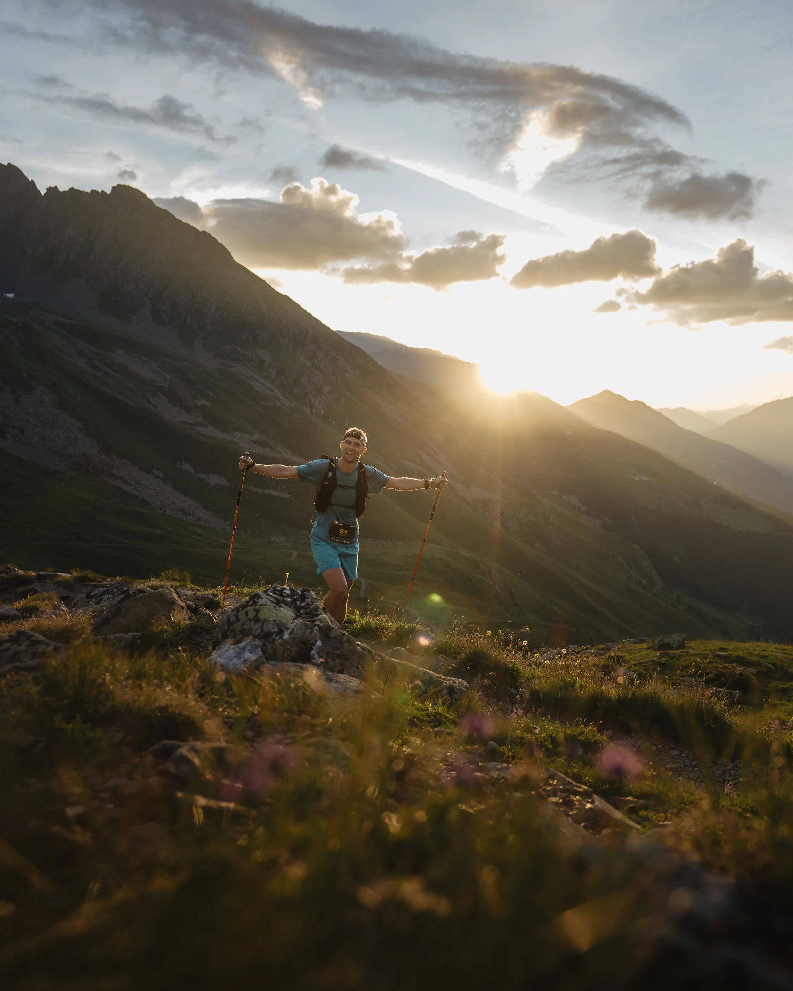 A smiling trail runner with poles in the mountains at sunset.