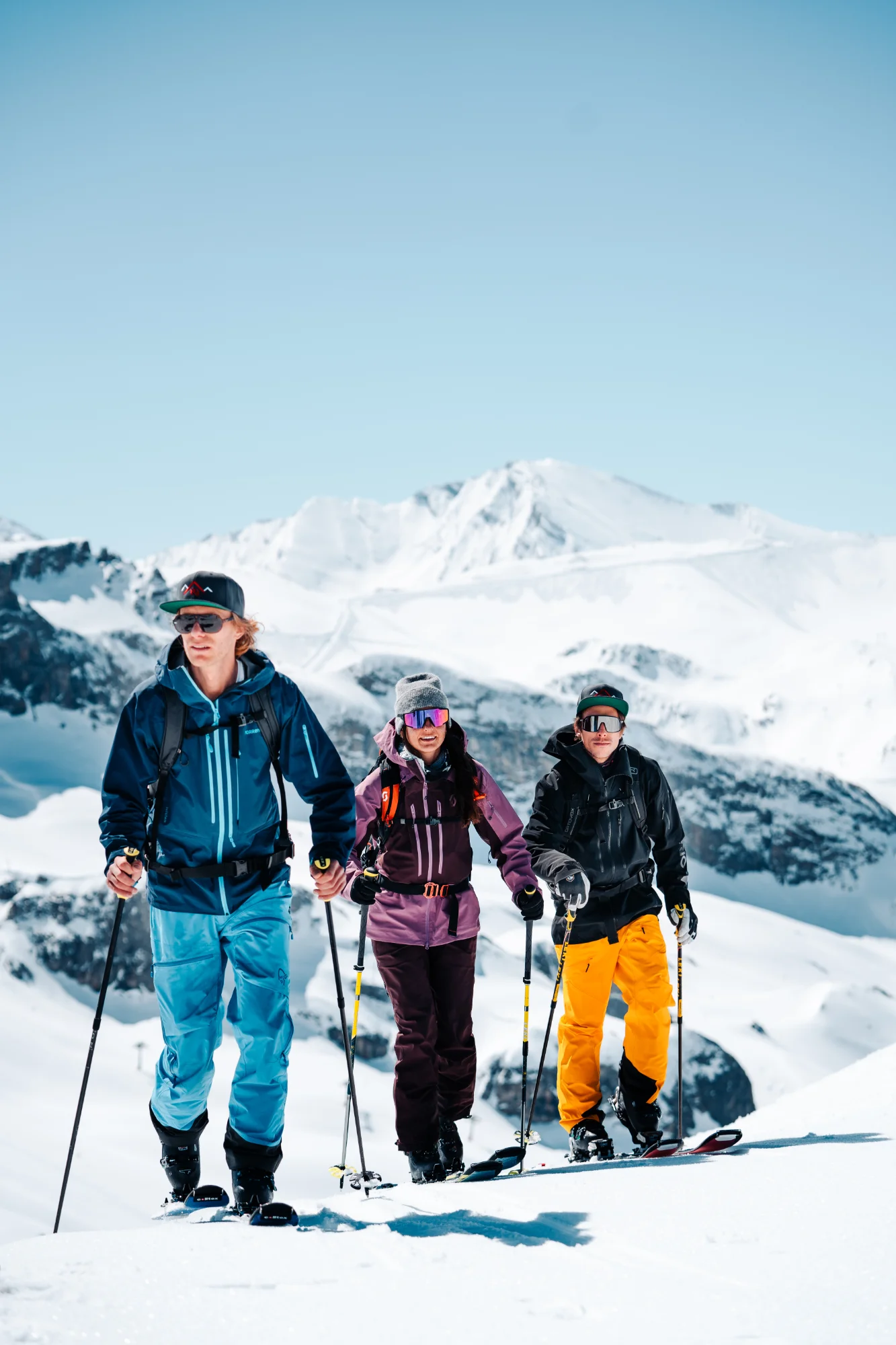Drei Skitourengeher steigen bei strahlendem Sonnenschein einen schneebedeckten Berg hinauf.