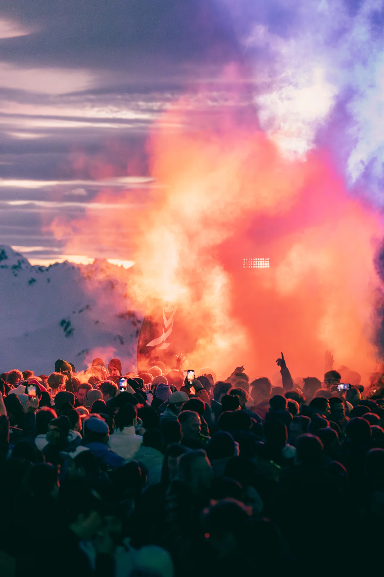 Zuschauer bei einem Outdoor-Konzert vor Bergen, eingehüllt in orange-roten Rauch von einer Leuchtrakete.
