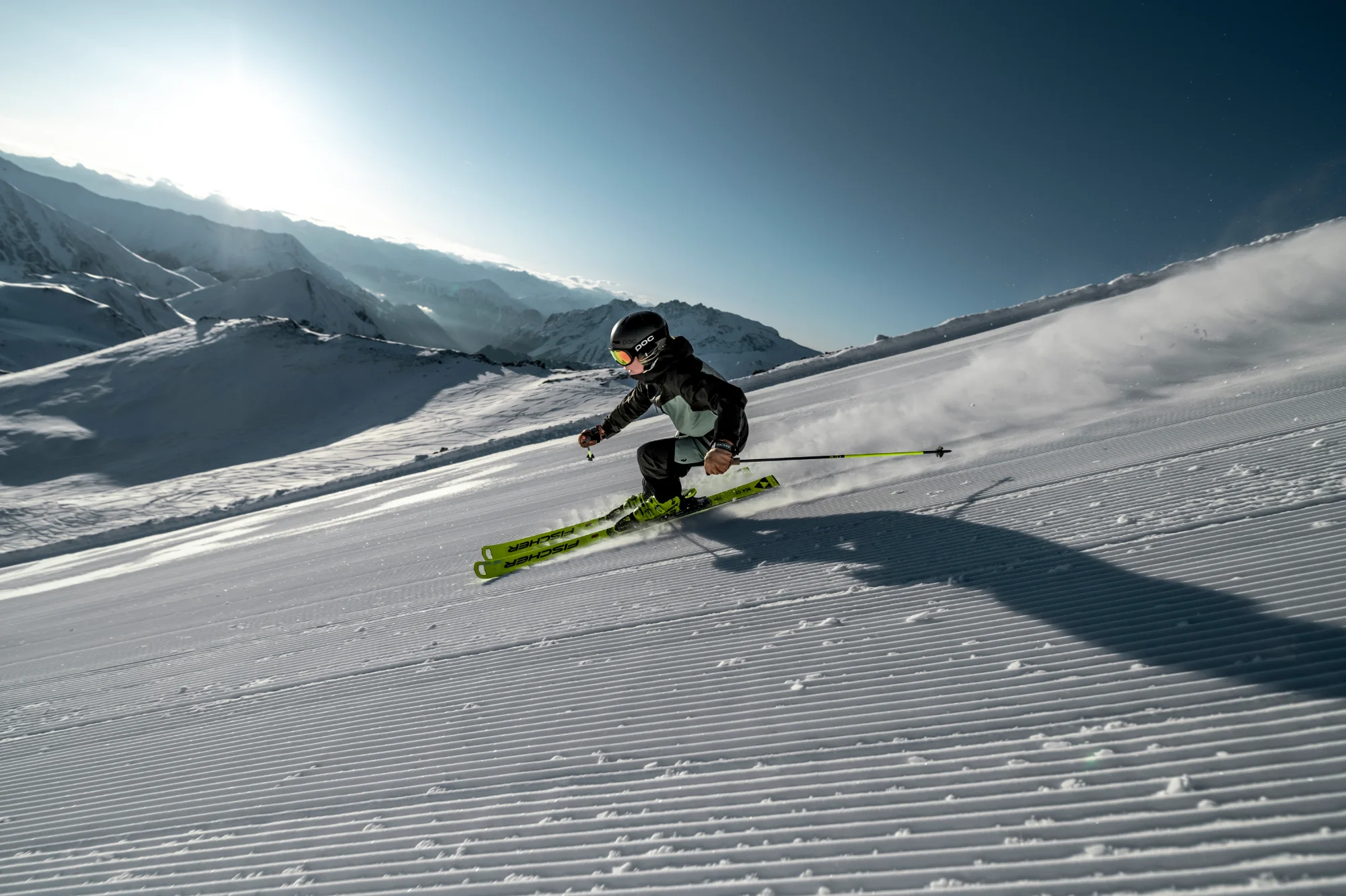 Ein Skifahrer gleitet auf einer präparierten Piste im Sonnenschein, mit Bergen im Hintergrund.