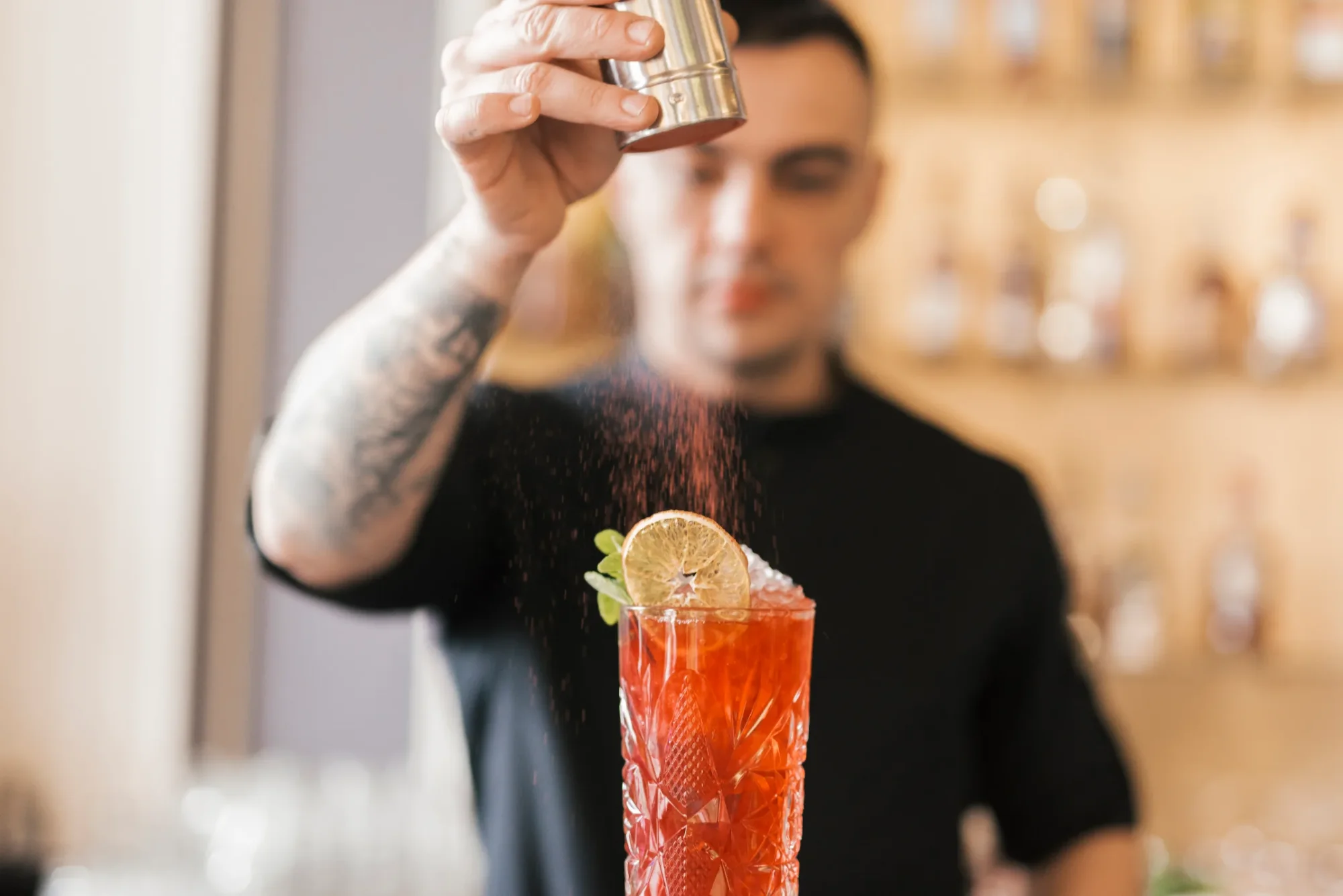 Barmann verziert roten Cocktail mit Puder aus Shaker, servierfertig in einem hohen Glas.
