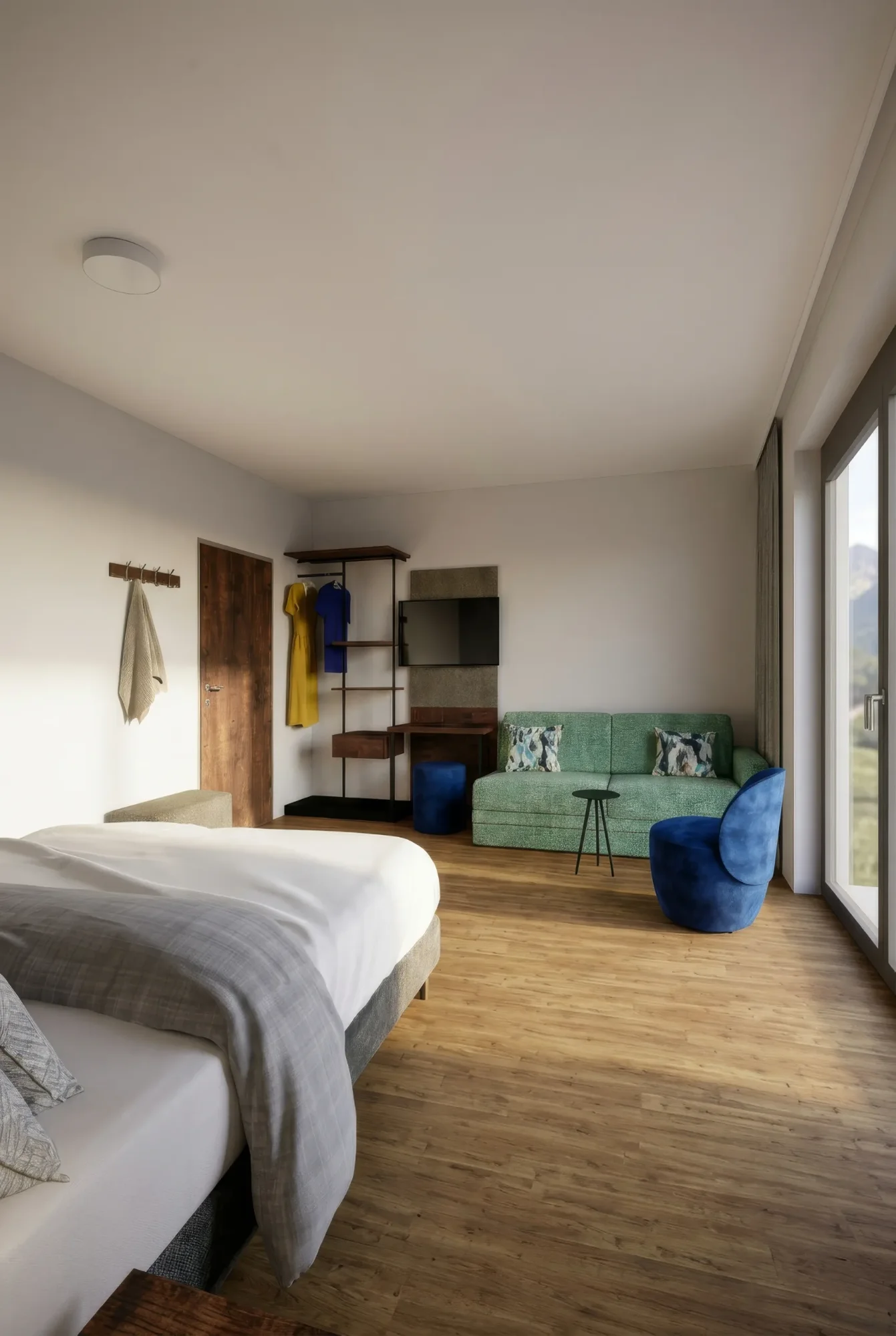 Helles Hotelzimmer mit Holzboden, großem Bett, grüner Couch, blauem Sessel und Fensterfront mit Bergblick.