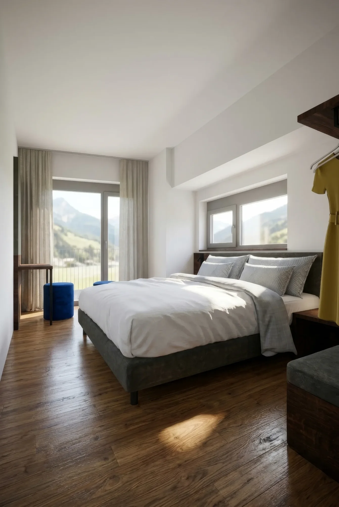 Helles, modernes Schlafzimmer mit großem Bett, Holzboden und Bergblick. Eine gelbe Robe hängt an der Wand.